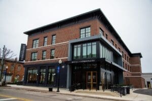 Hotel Versailles, a three-story brick hotel with large windows, black awnings, and a covered entrance, situated along a street corner on an overcast day.